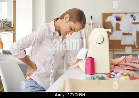 La donna stanca che lavora come sarto e ha una cattiva postura soffre di mal di schiena Foto Stock