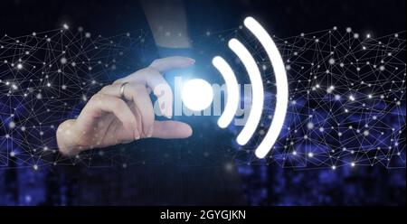 Concetto di connessione di rete aziendale e Wi-Fi in città. Hand hold digital ologram Wi Fi segno sulla città scuro sfondo sfocato Foto Stock