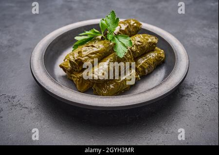 Tradizionale dolma mediorientale piatto o tolma, con prezzemolo in piatto nero su sfondo di legno scuro. Primo piano Foto Stock
