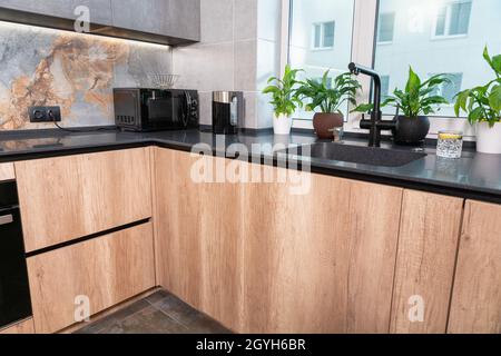 All'interno di un moderno appartamento cittadino in un alto edificio, si trova una cucina arredata con mobili in pietra e mobili in legno con elettrodomestici Foto Stock