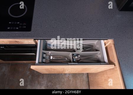 Vista dall'alto in basso di un banco da cucina in pietra grigia con cassetto di posate aperto che mostra gli utensili da cucina ordinatamente disposti in scomparti con copyspace Foto Stock
