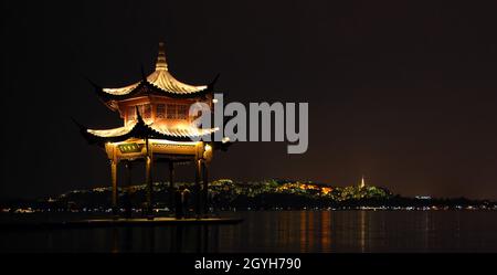 West Lake, Hangzhou, provincia di Zhejiang in Cina. Un padiglione costruito sulle acque del Lago Ovest di Hangzhou. Vista notturna con Baoshi Mountain dietro. Foto Stock