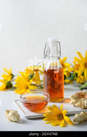 Topinambour sciroppo di topinambour del carciofo di Gerusalemme in ciotola e bottiglia su sfondo bianco. Formato verticale. Sostituto dello zucchero per dolci vegani crudi. Foto Stock