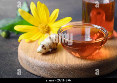 Sciroppo di carciofo di Gerusalemme in ciotola, fiori e radice su sfondo bianco. Primo piano. Foto Stock