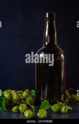 Bottiglia di birra marrone retrò su sfondo di pietra con luppolo pianta. Bevanda scura ancora vita Foto Stock