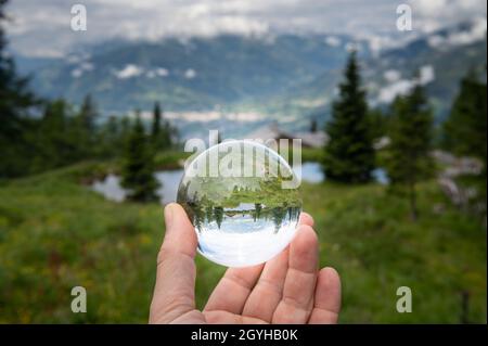 Sfera di vetro tenuta a mano davanti al pascolo, giorno nuvoloso in estate, alpi in Tirolo Orientale (Austria) Foto Stock