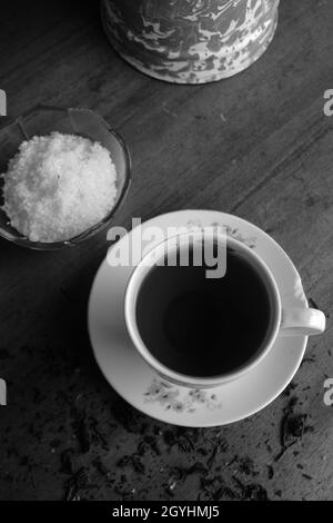 Primo piano verticale in scala di grigi di una tazza e piattino con tè e una ciotola di zucchero Foto Stock