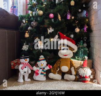 Giocattolo souvenir snowmen e Santa peluche Tiger stand sotto un albero di Natale artificiale decorato. Vacanze invernali accoglienti. Tiger morbido giocattolo come simbolo di 2022 Foto Stock