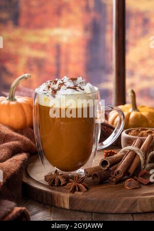 Latte di zucca speziata con bastoni di cannella e zucche da una finestra con sfondo autunno Foto Stock