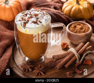 Latte di spezie di zucca con bastoncini di cannella su un piatto di legno e mini zucche sullo sfondo Foto Stock