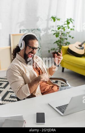 entusiasta freelance ispanico in cuffie urla mentre ascolti musica vicino al laptop Foto Stock
