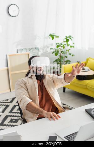 un uomo ispanico stupito che si sta gestendo mentre si gioca con un visore vr nel salotto di casa Foto Stock