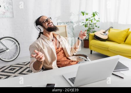 contento latino freelance in cuffie ascoltare musica vicino al portatile a casa Foto Stock