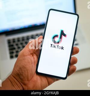 Vista ravvicinata della mano con smartphone e Tik Tok ​logo sul display. Notebook in background. Nuova tecnologia, social media, rete, comunicazione, conc Foto Stock