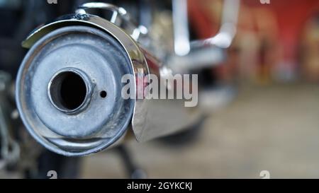 Foto del tappo terminale del silenziatore del motociclo con sfondo sfocato dell'officina. Foto dei pezzi di ricambio a due ruote. Foto Stock