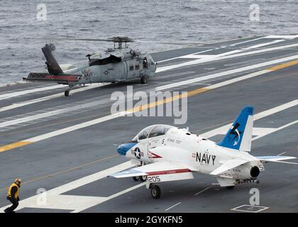 OCEANO ATLANTICO (Gen. 18, 2020) Un T-45 Goshawk, assegnato a Air Test and Evaluation Squadron (VX) 23, transita sul ponte di volo USS Gerald R. Ford (CVN 78) come elicottero MH-60 Sea Hawk, assegnato ai 'tridenti' di Helicopter Sea Combat (HSC) 9 si prepara al decollo. Ford sta attualmente conducendo il test di compatibilità degli aeromobili per testare ulteriormente i suoi sistemi di lancio degli aeromobili elettromagnetici (EMALS) e Advanced Arresting Gear (AAG). (STATI UNITI Foto Navy di Seaman Zack Guth, specialista della comunicazione di massa) Foto Stock