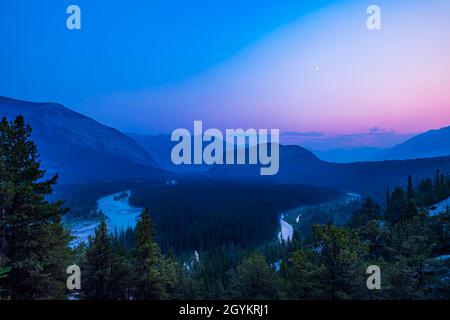 Crepuscolo blu con una luna crescente ceretta, sopra la Valle del Bow, Banff, Alberta, in una serata con l'aria piena di fumo di abete bosco B.C. Foto Stock
