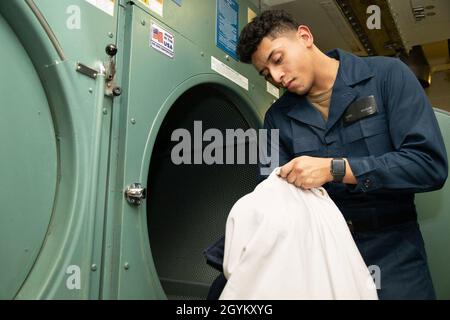 OCEANO ATLANTICO (Gen. 24, 2020) Seaman Isreal Salazar, da Los Angeles, assegnato al reparto di approvvigionamento di USS Gerald R. Ford (CVN 78), recupera le giacche malate da una dyer industriale di bordo della nave nella stanza di operazioni di lavanderia di Ford. Ford sta attualmente conducendo test di compatibilità degli aeromobili. (STATI UNITI Foto Navy di Seaman Zack Guth, specialista della comunicazione di massa) Foto Stock