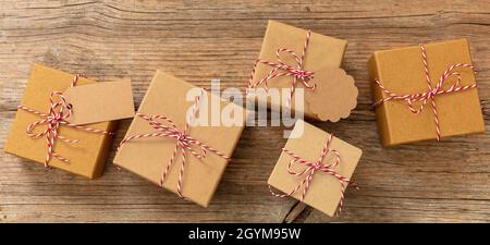 Scatole regalo di Natale, carta kraft marrone festa presenta con arco legato filo rosso bianco a strisce su sfondo tavola di legno, vista dall'alto. fai da te in casa eco Foto Stock