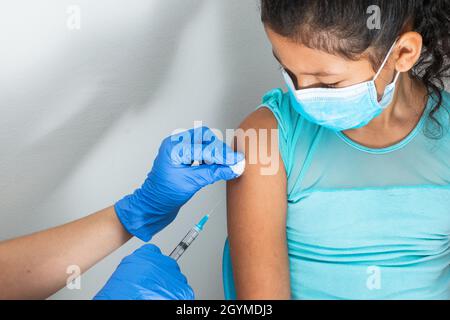 l'infermiera dei bambini pulendo il sangue con la lana di cotone dopo la somministrazione dell'iniezione nel braccio della ragazza marrone. il medico iniettando il vaccino contro covid-19. influenza vacci Foto Stock