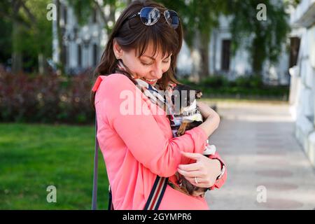 Felice giovane donna caucasica che abbraccia il suo cane piccolo, russo Toy o russo Toy Terrier, vestito in tuta d'autunno. Concetto di amore per gli animali domestici Foto Stock