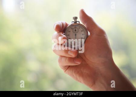 La mano di un uomo tiene un classico cronometro meccanico analogico in metallo cromato, su uno sfondo verde sfocato. Foto di alta qualità Foto Stock