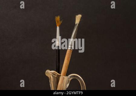 Vecchie spazzole per pittura artistica usate in vaso di vetro terto. Vita morta. Composizione minimalista con sfondo nero. Foto Stock