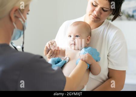 Femmina medico che esamina la bambina piccola sorridente, tenuta dalla madre Foto Stock