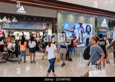Gli amanti dello shopping passano accanto al negozio e logo Adidas, il marchio sportivo tedesco della multinazionale, a Hong Kong. Foto Stock