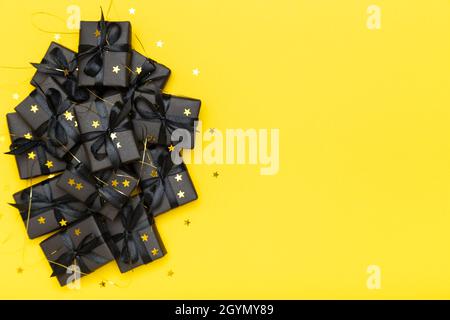 Scatole regalo nere con nastri neri e stelle con glitter dorate che brillano su sfondo giallo brillante e ricco. Black Friday vendita piatto, vista dall'alto, spazio copia Foto Stock