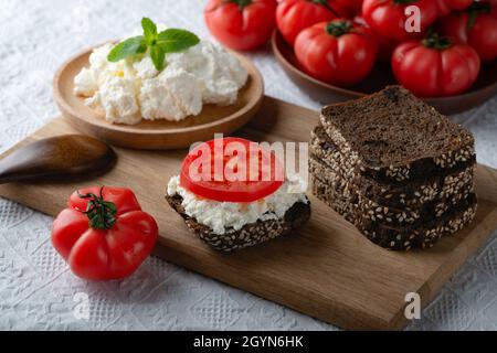 Fette di pane di segale con formaggio casereccio e pomodori su piatto di legno Foto Stock