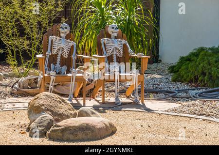 Due scheletri di Halloween si siedono su due sedie a prato nell'anno anteriore di una casa in un quartiere residenziale. Foto Stock