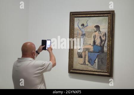 Il visitatore che indossa una maschera usa uno smartphone per fotografare il dipinto "Young Acrobat on a Ball" di Pablo Picasso (1905) esposto alla mostra "icone di arte moderna della collezione Morozov" della Fondazione Louis Vuitton a Parigi, Francia. La mostra si svolge fino al 22 febbraio 2022. Foto Stock