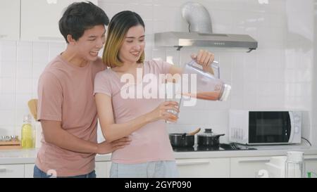 Felice Asian giovane coppia di famiglia marito e moglie godendo di bere fresco succo di frullato di mela in cucina a casa. Donna versato succo dal frullatore per Foto Stock