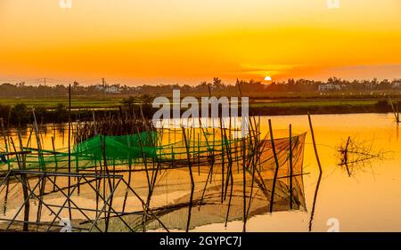 L'acqua è come il vetro mentre il sole tramonta sulle rive del fiume Bon con una trappola da pesca rotonda nel mezzo. Foto Stock