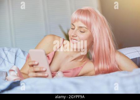 Bella donna testi sul telefono cellulare appoggiati a portata di mano in letto confortevole a. Foto Stock