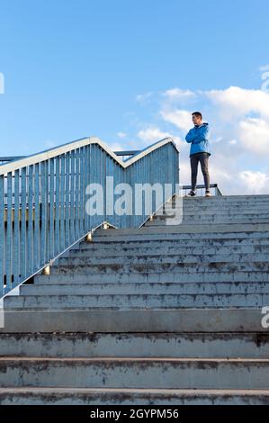 Un giovane sportivo si trova in cima alla piattaforma di osservazione e guarda in lontananza. Il concetto di superare le difficoltà, salire in cima. Foto Stock