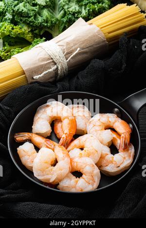 Spaghetti al parmigiano aromatizzato all'aneto, ingredienti per la cottura dei gamberi, su padella di ferro, su fondo tavola di legno nero Foto Stock