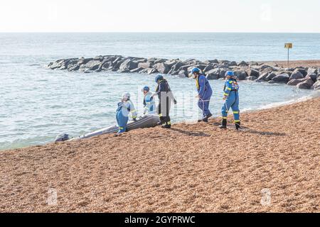 Guardie costiere e un ufficiale di polizia che tirano un gommone usato dagli immigrati clandestini sulla spiaggia di Folkestone, nel Kent. Foto Stock