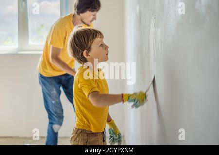 L'uomo con suo figlio fa delle riparazioni a casa, insegna ai bambini ad intonacare le pareti con una spatola nelle mani Foto Stock