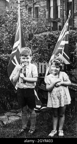 I bambini piccoli hanno orgogliosamente bandiere del Regno Unito per celebrare l'incoronazione del monarca britannico, re Giorgio VI, il 12 maggio 1937 Foto Stock