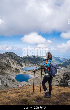 Escursionista di montagna con abiti colorati e bastoncini da passeggio in piedi su una scogliera e guardando gli splendidi laghi ghiacciai sulla montagna di Rila Foto Stock