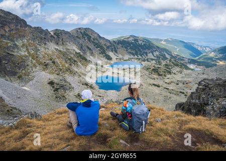 Due escursionisti di montagna in abiti colorati seduti su una scogliera e guardando gli splendidi laghi ghiacciai sul monte Rila durante l'escursione sul picco Musala Foto Stock