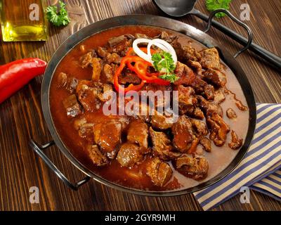 Goulash di manzo in una padella con peperoncino rosso su legno Sfondo Foto Stock