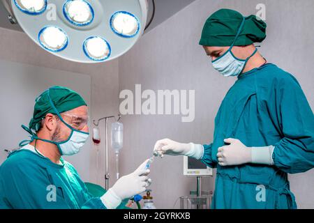 il medico e l'infermiere che tengono la siringa e il flacone della medicina di anestesia da preparare per il paziente nella sala operatoria di emergenza prima dell'intervento chirurgico all'ospedale. Foto Stock