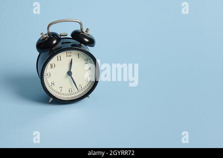 Sveglia nera con la metà della mezzanotte sul quadrante dell'orologio. Natale e Capodanno concetto isolato su sfondo blu con poliziotto Foto Stock