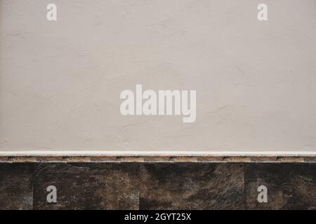 Parete in gesso bianco calcarato con finitura in pietra, pannello battiscopa in ceramica, dettaglio architettura sfondo Foto Stock