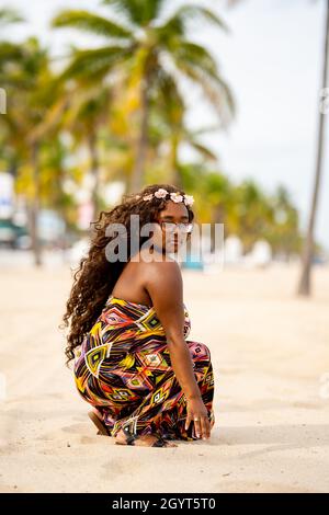 Bella giovane modello femminile multirazziale in posa in un abito colorato in un ambiente tropicale Foto Stock