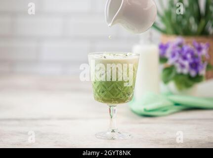 Tè freddo Matcha verde con cubetto di ghiaccio e latte. Concetto di cibo sano. Versare il latte in un bicchiere di tè verde. Con spazio di copia per il testo. Foto Stock