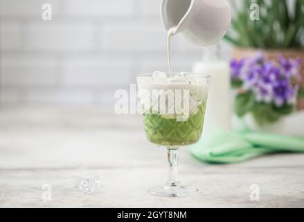 Tè freddo Matcha verde con cubetto di ghiaccio e latte. Concetto di cibo sano. Versare il latte in un bicchiere di tè verde. Con spazio di copia per il testo. Foto Stock